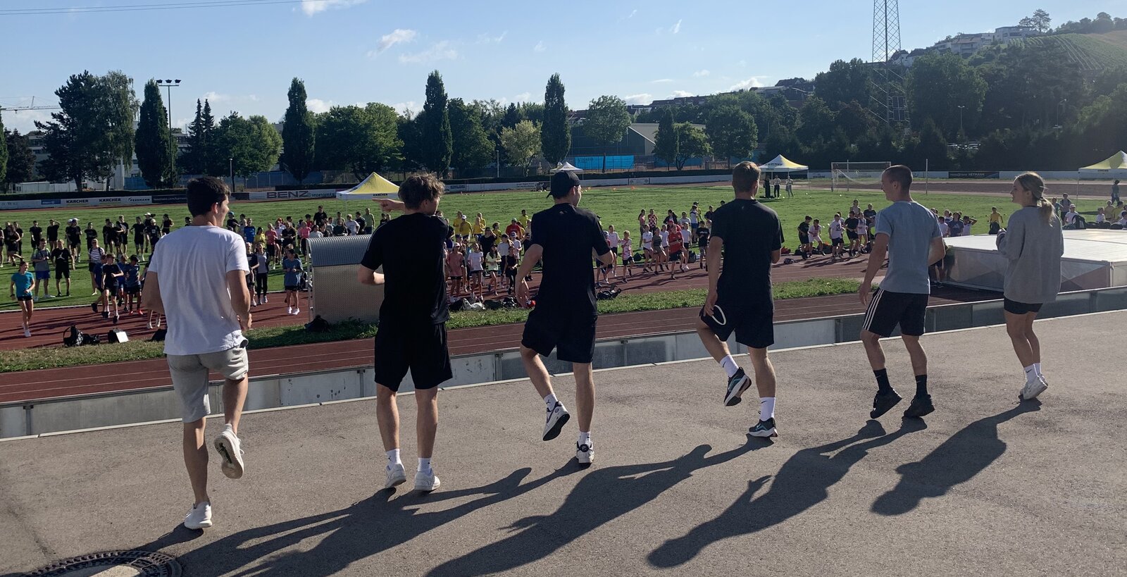 Sechs Schüler*innen, die sich aufwärmen vor einem Sportplatz.